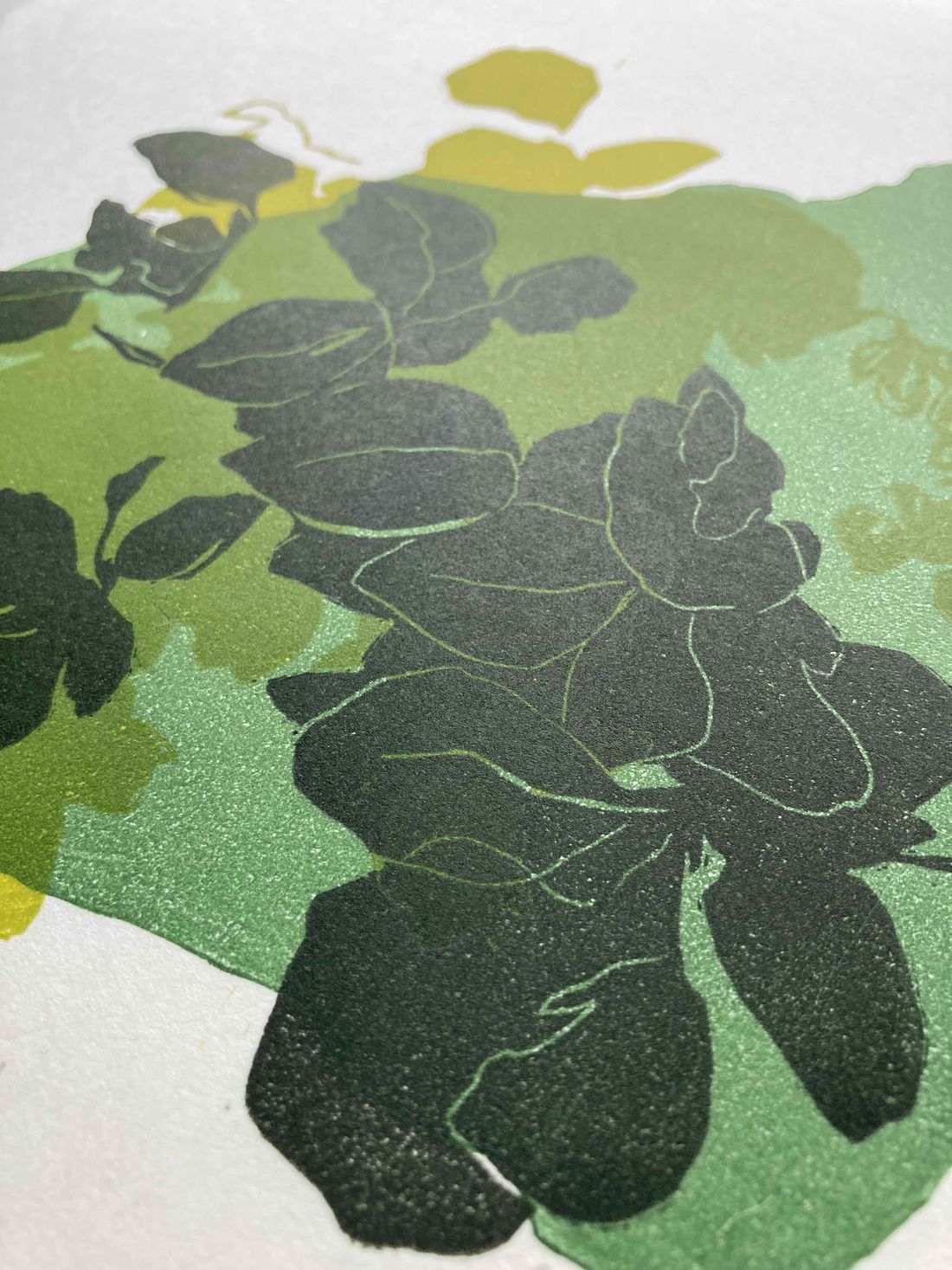 Close-up of a layered linocut print: dark green leaves over washes of green and yellow ink on textured paper