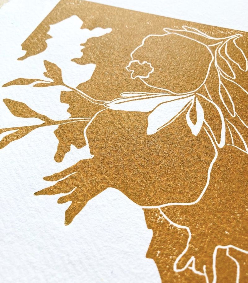 Close-up of an ochre linocut print with leaves and a flower drawn in white line
